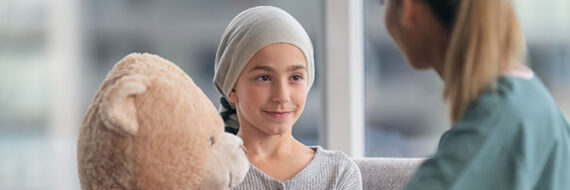 Child with cancer holding teddy bear looking at therapist